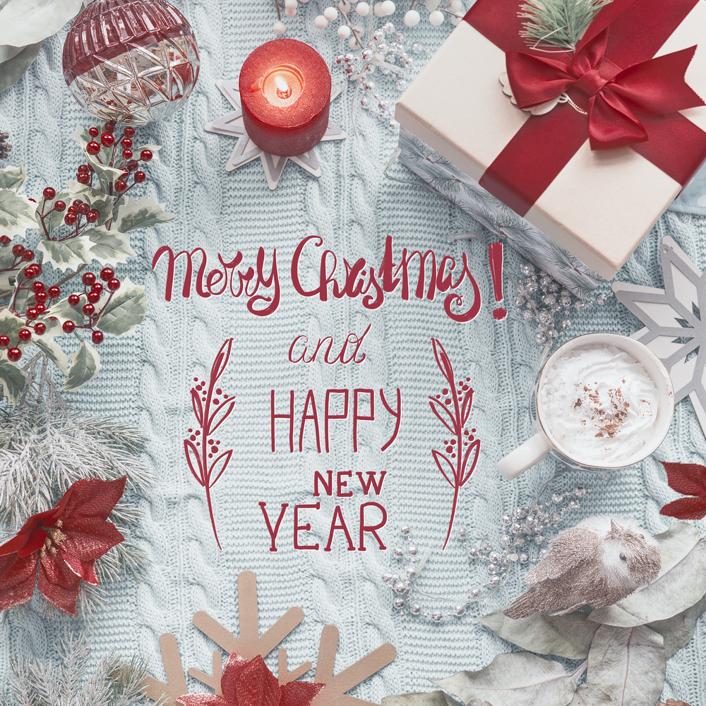 Merry Christmas and Happy New Year text on blue knitted blanket with red vintage Christmas decoration, present gift box, burning candles and  cup of cappuccino . Top view. Flat lay. Greeting card