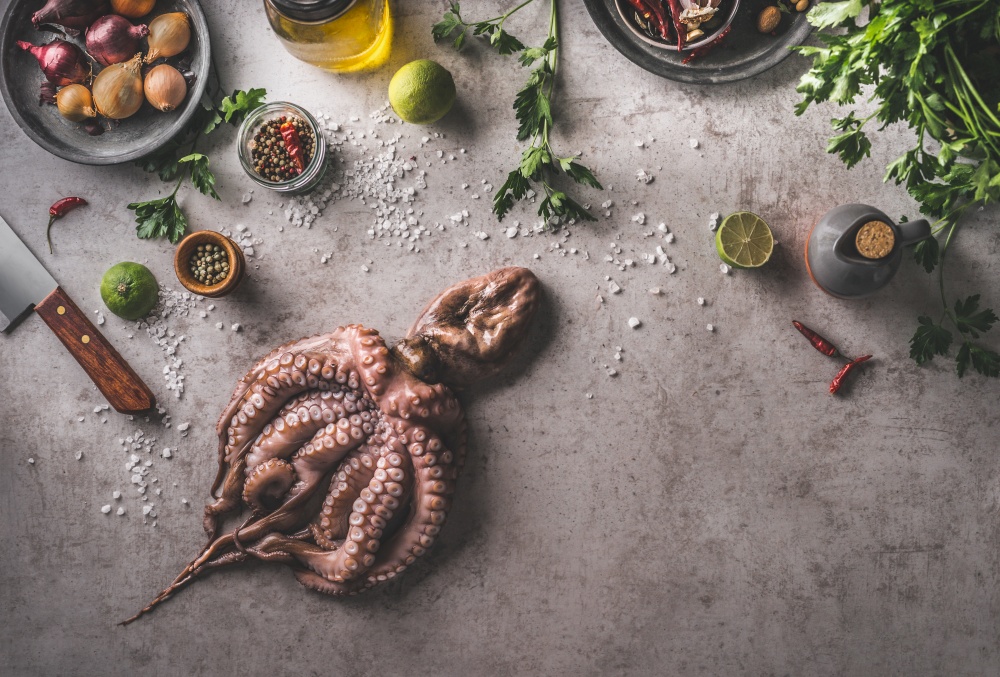 Cooking preparation of Octopus with fresh ingredients and kitchen equipment , herbs, lime, onion, salt, spices. Fresh food concept on dark concrete background. Top view