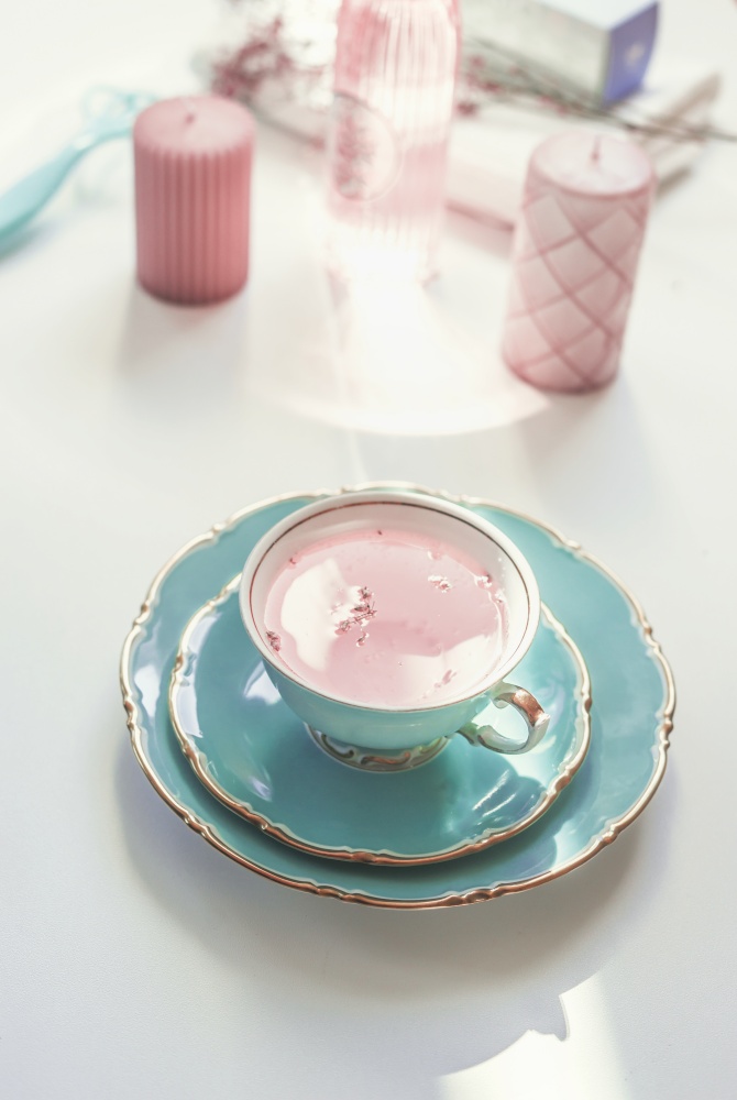 Turquoise porcelain cup with pink flowers tea on light table with candles and cosmetics. Female morning routine