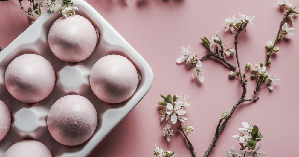 Easter eggs in white holder with cherry blossom branches on pink background, top view