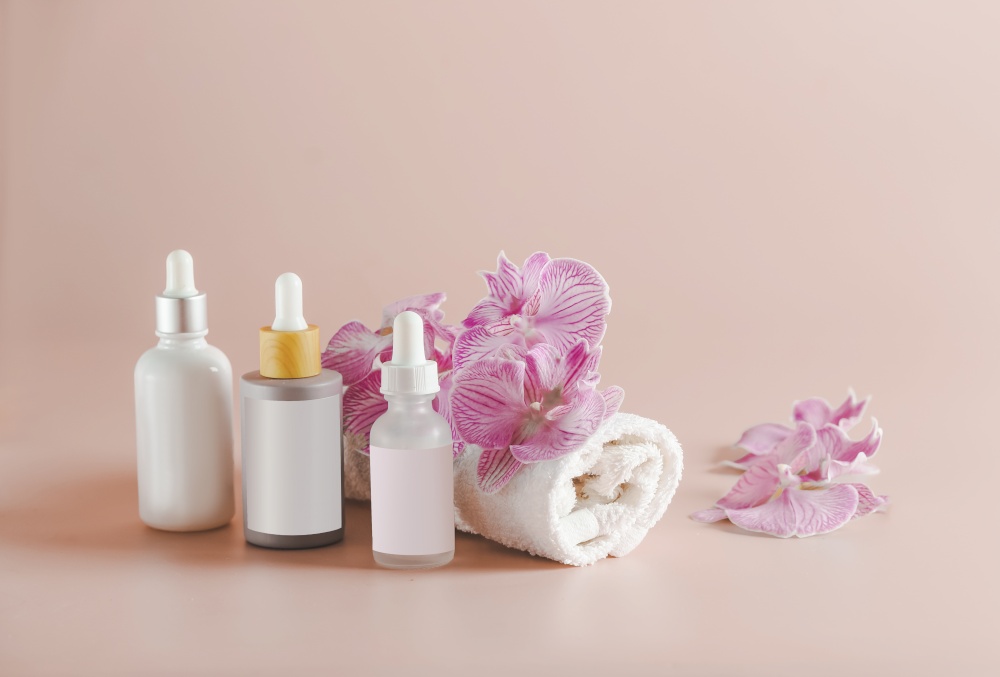 Beauty products setting with towel, cosmetic bottles and orchid flowers at pink background
