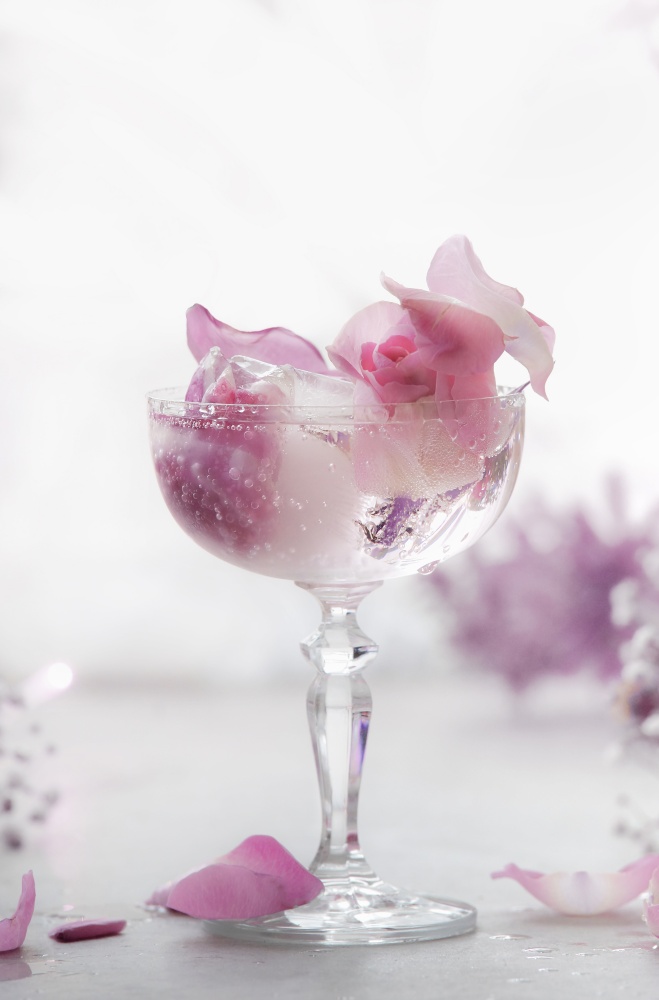 Fancy drink in wide champagne glass with pink flowers and ice cubes