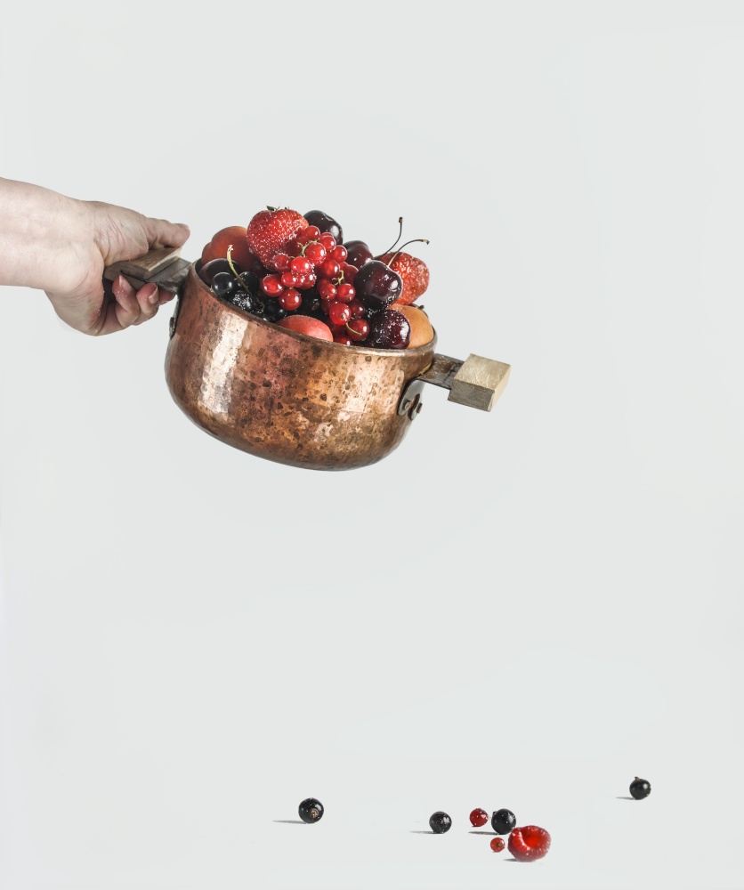 Women hand holding cooking pot with various berries on white background, front view
