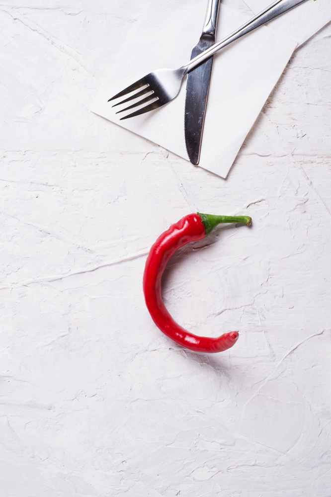 hot chili pepper with fork and knife at white table. copy space. flat lay