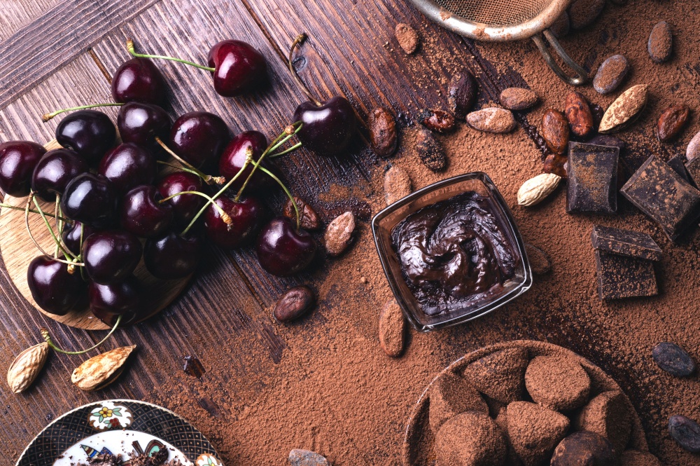 art background with healthy delicious dark truffles, chocolate  and  ingridients:  natural cocoa beans,  powder, chocolate, almonds  nuts and  ripe cherry. healthy sweets concept. flat lay