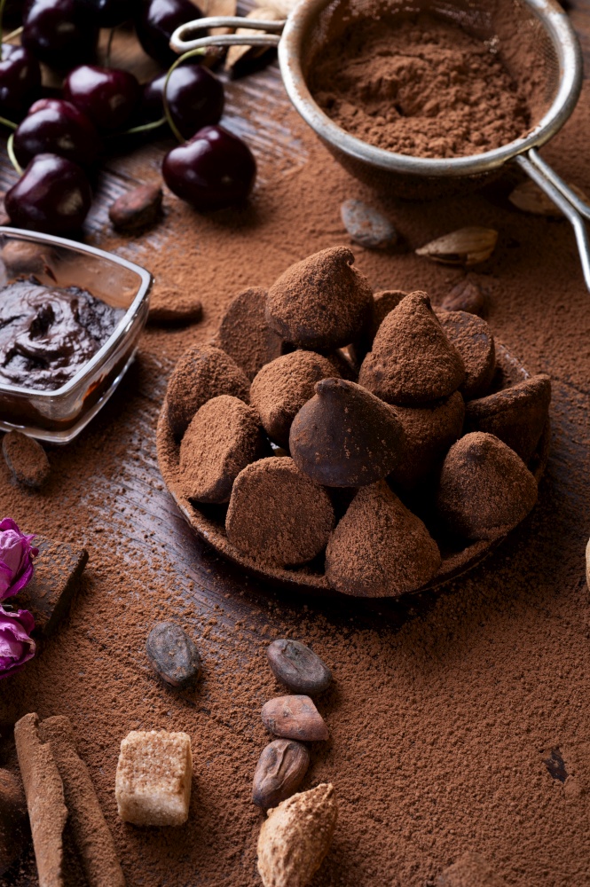 art background with healthy delicious dark truffles, chocolate  and  ingridients:  natural cocoa beans,  powder, chocolate, almonds  nuts and  ripe cherry. healthy sweets concept.