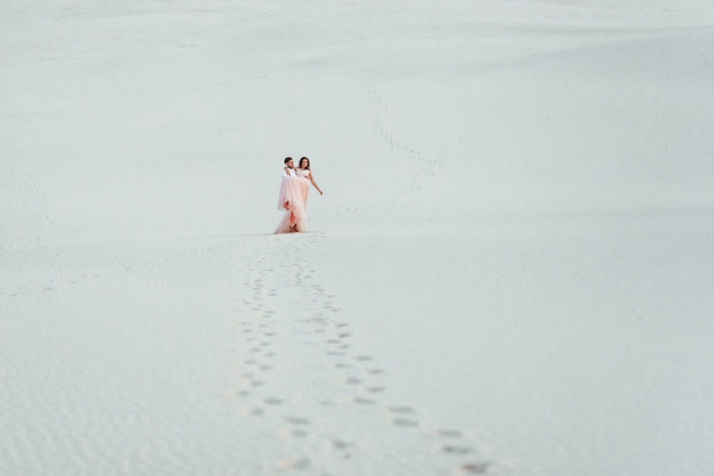 young couple a guy in black breeches and a girl in a pink dress are walking along the white sand of the desert