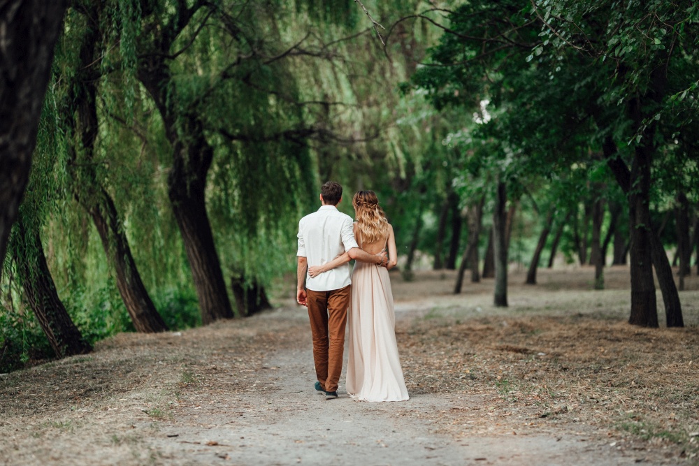 a guy and a girl are walking along the banks of a wild river overgrown with willows and forest