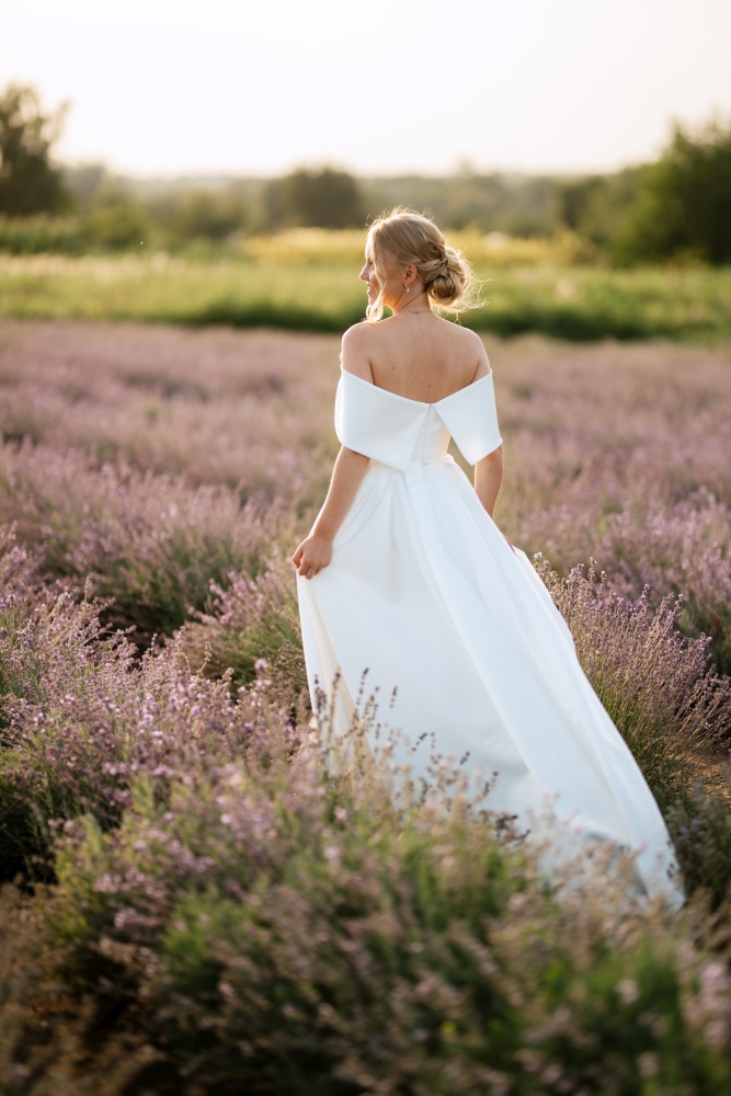 the bride in a white dress walks on the lavender field