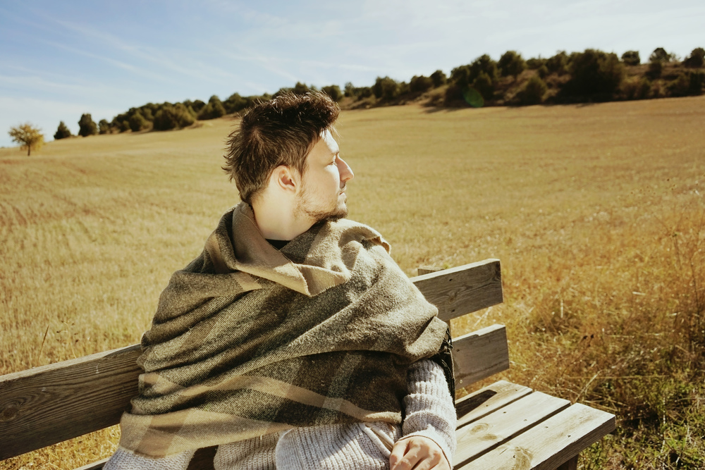 Side face of a sitting young man with the eyes closed enjoying in calm the morning autumn sun in a yellow field
