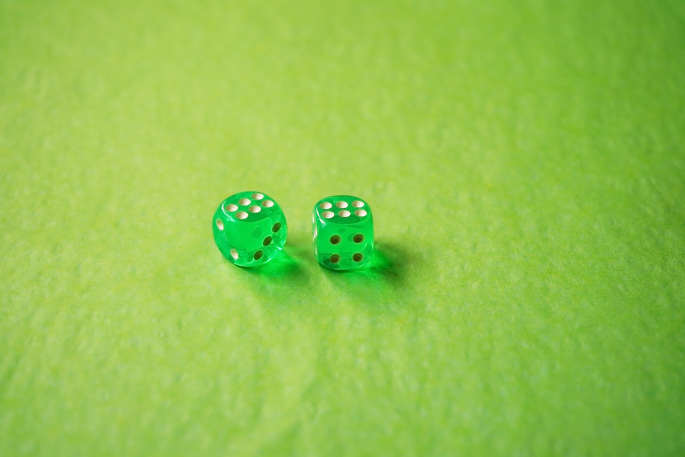 A vibrant monochromatic macro with depth of field about two green glass gambling dice with two lucky number six on green background.