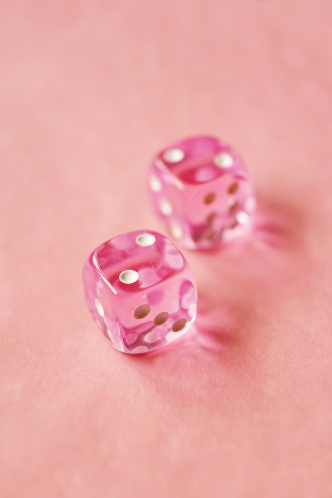 A vibrant monochromatic macro with depth of field about two pink glass gambling dice with two unlucky number two on pink background.