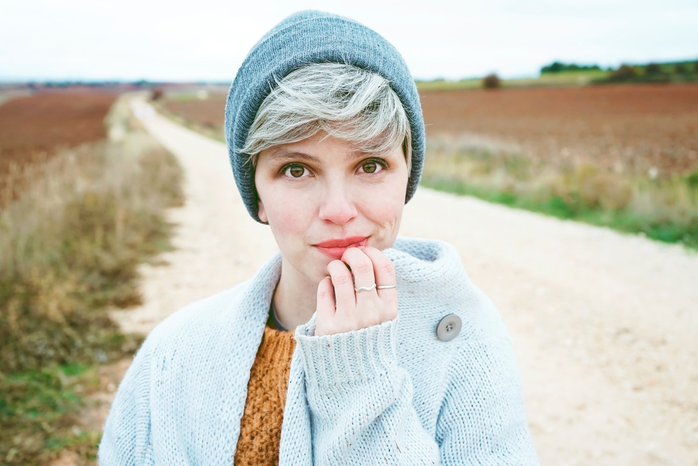 Woman with short and gray hair is alone in the beggining of a rural path in a cold autumn day