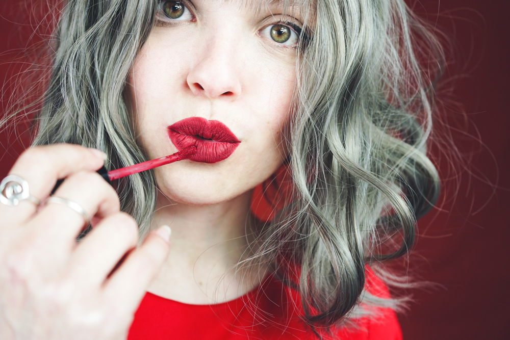 Young woman makeup her lips with a red matte lipstick