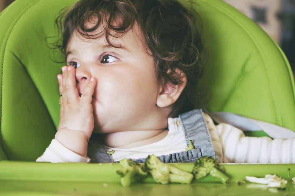 Baby eating food in her green highchair