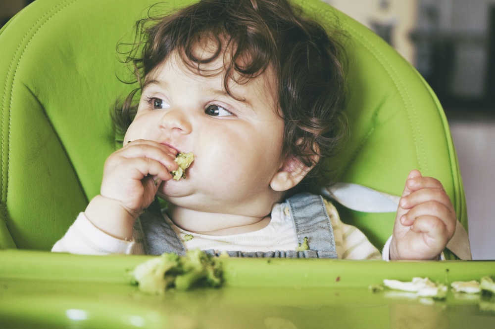 Baby eating food in her green highchair