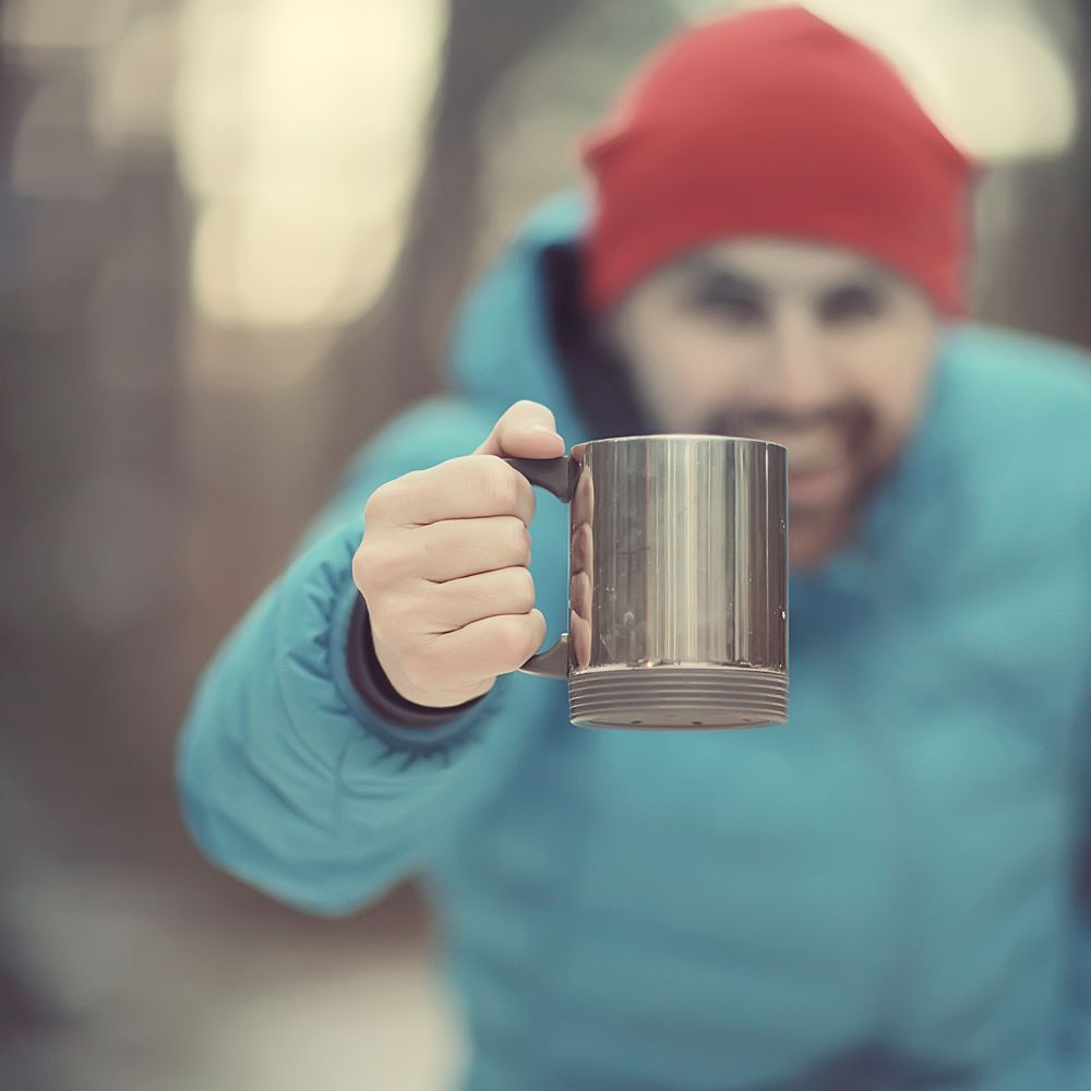 traveler in a winter forest drinks a hot drink and holds a cup