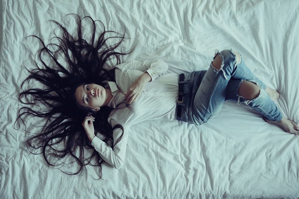 Brunette beautiful young adult with long hair lying on the bed