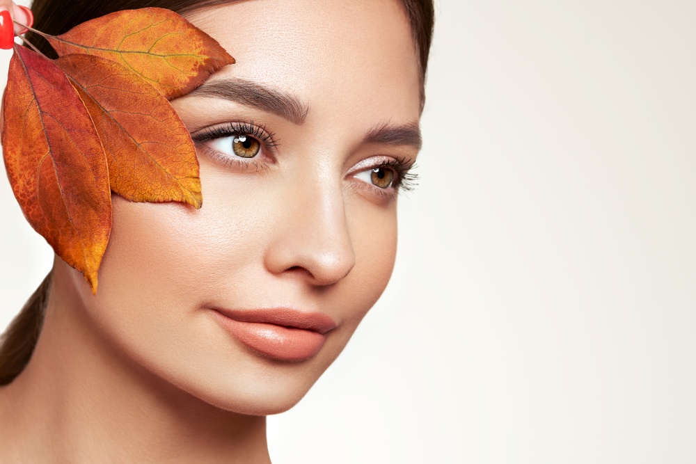 Portrait of beautiful young woman with autumn  leafs. Healthy clean fresh skin natural make up beauty eyes and shiny plump lips