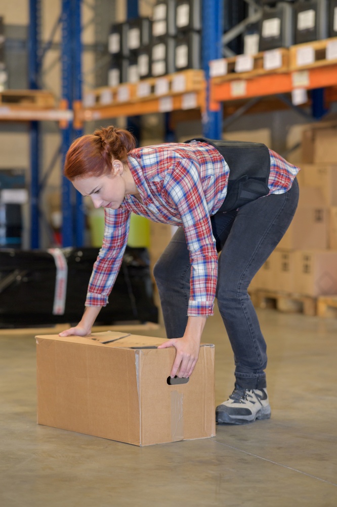 warehouse manager picking up cardboard box in a large warehouse