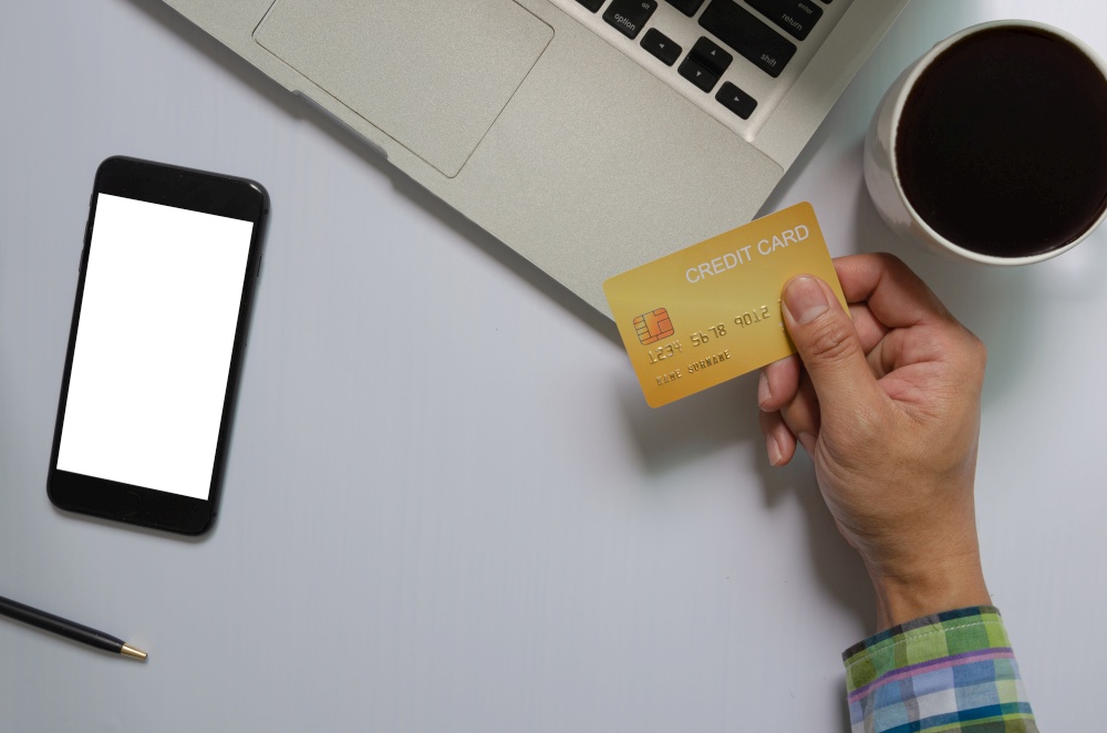 top view of a man holding a credit card Mobile phone mock up blank white screen and computer and coffee Business communication technology, online shopping concept.
