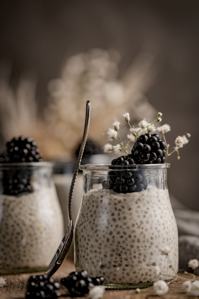 Chia pudding with blackberries, three portions in glass jars on a dark table.