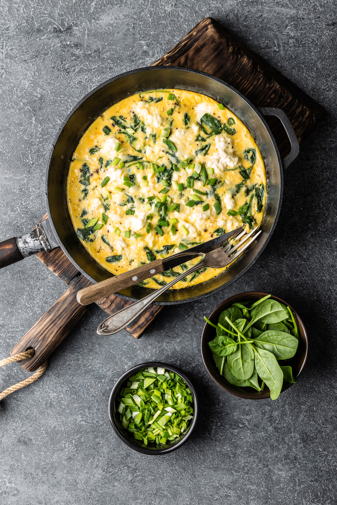 omelette with spinach and cheese in a pan on the concrete background top view