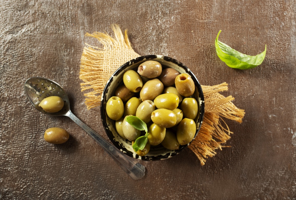 Green olives and basil leaves on wooden background