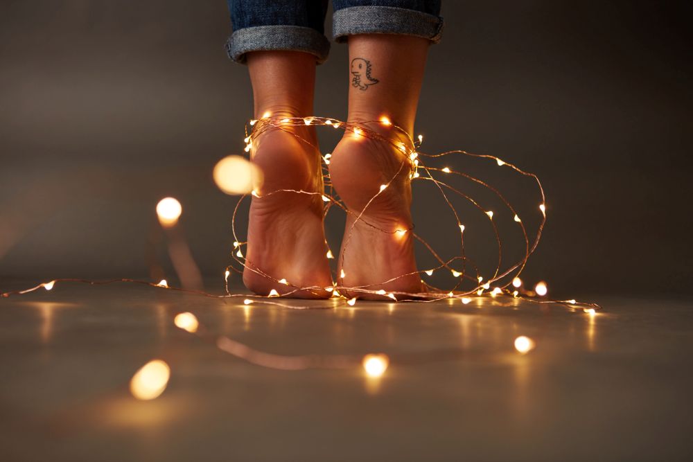 Tattoo feet of the woman decorated with a festive Christmas garland on a dark background. Holiday concept. Feet of the woman decorated with a festive Christmas garland on a dark background.