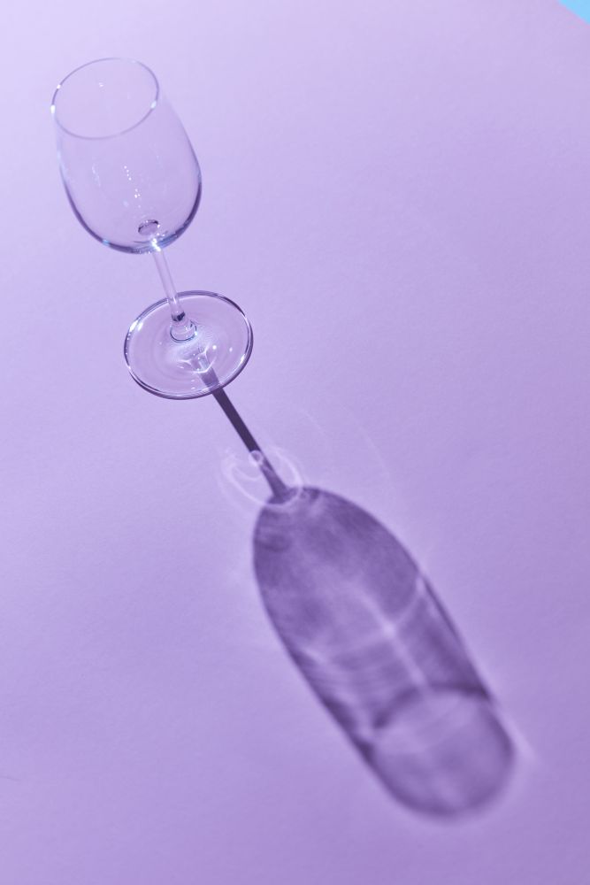 A glass of wine on a purple background with a falling shadow from a glass. wineglass sunlight and shadow on a purple background