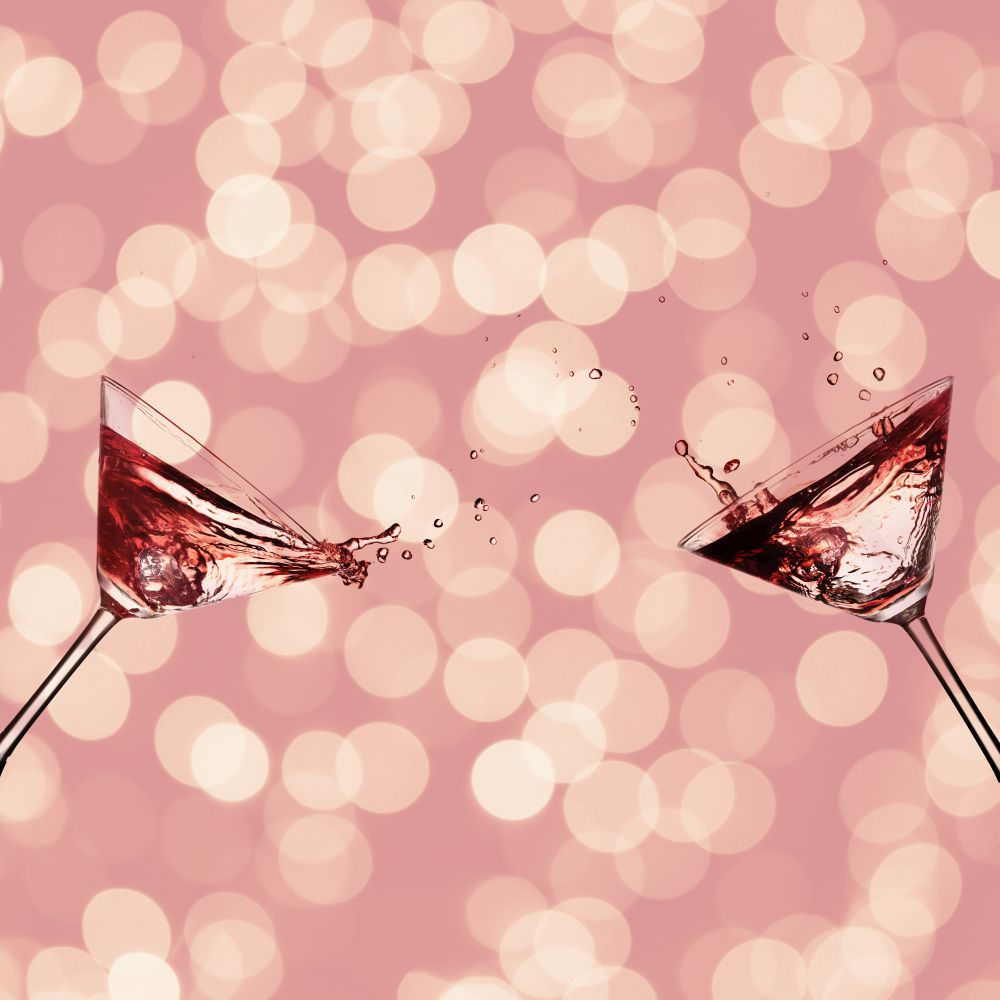Two glasses with cocktail for martini with splash on a pink background bokeh. Two glasses with cocktail
