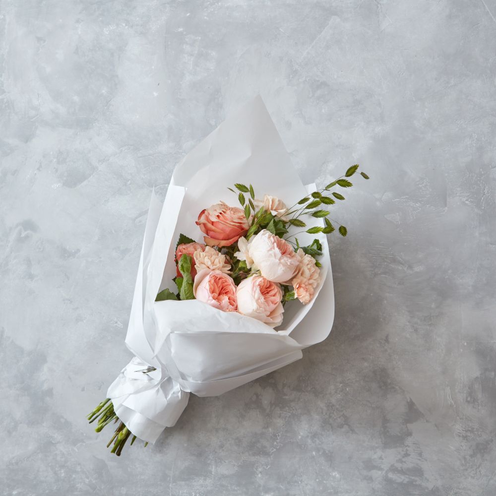 Wedding bouquet of peach roses with white paper on a gray stone background. Beautiful peach roses