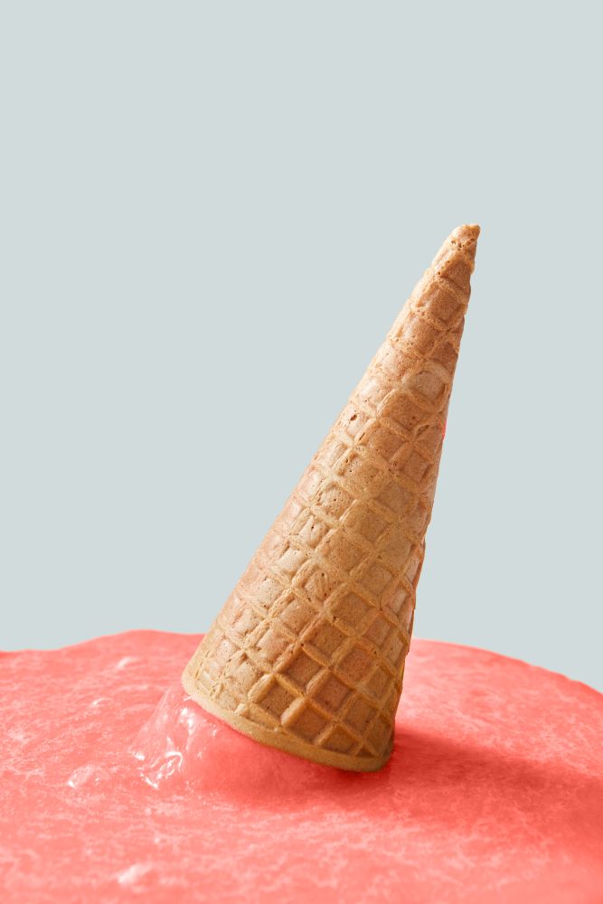 Meltdown of ice cream in a color of the year 2019 Living Coral pantone on a gray background. Falling crispy waffle cone of ice cream. Place for text.. Waffle cone with melted ice cream in a color of the year 2019 Living Coral pantone on a gray background with copy space.