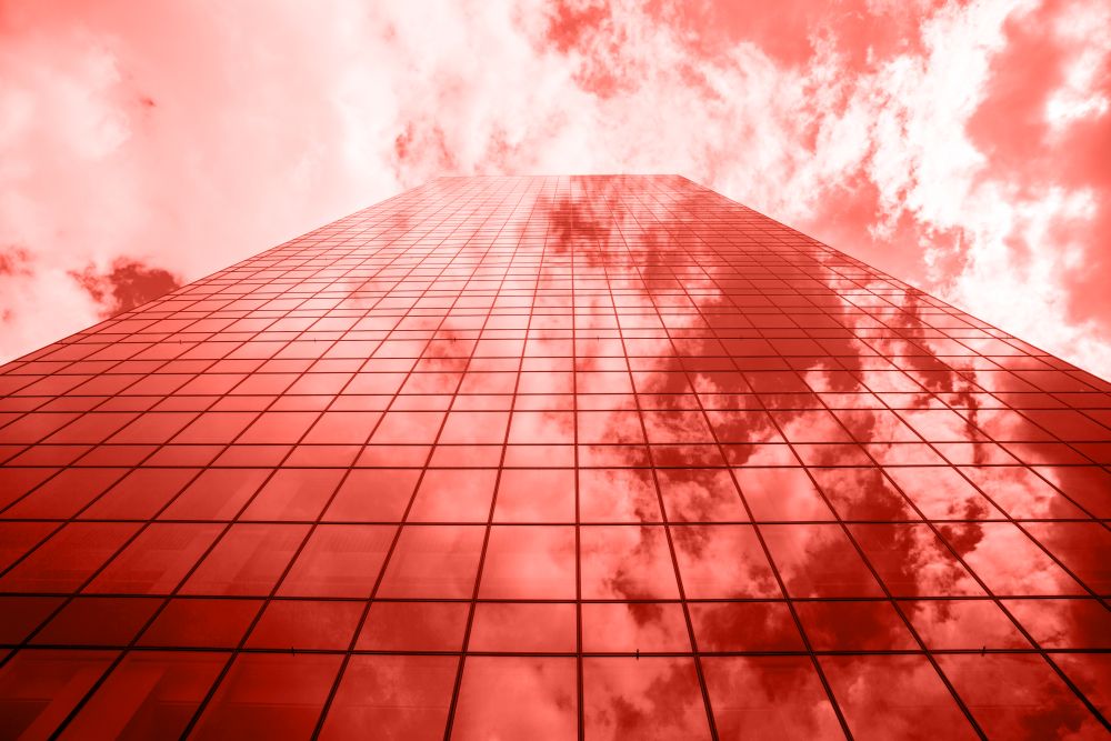 Perspective of urban glass business skyscraper with shadows and reflections of sky clouds on a shiny surface in a fashionable pantone trendy color of spring-summer 2019 season.. Glass facade of modern business building with reflections and shadows in a color of the year 2019 Living Coral pantone on a background oh cloudy sky.