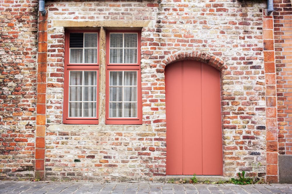 Freshly painted door on old European stone house of Bruges, Belgium in a color of the year 2019 Living Coral Pantone.. Facade brick old wall with painted door in a trendy color of the year 2019 Living Coral Pantone.