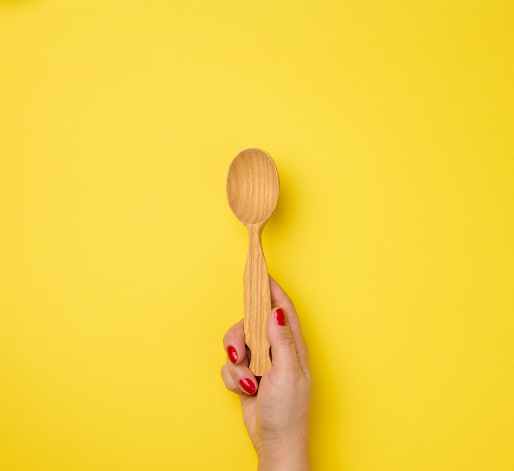 female hand holding empty wooden spoon on yellow background
