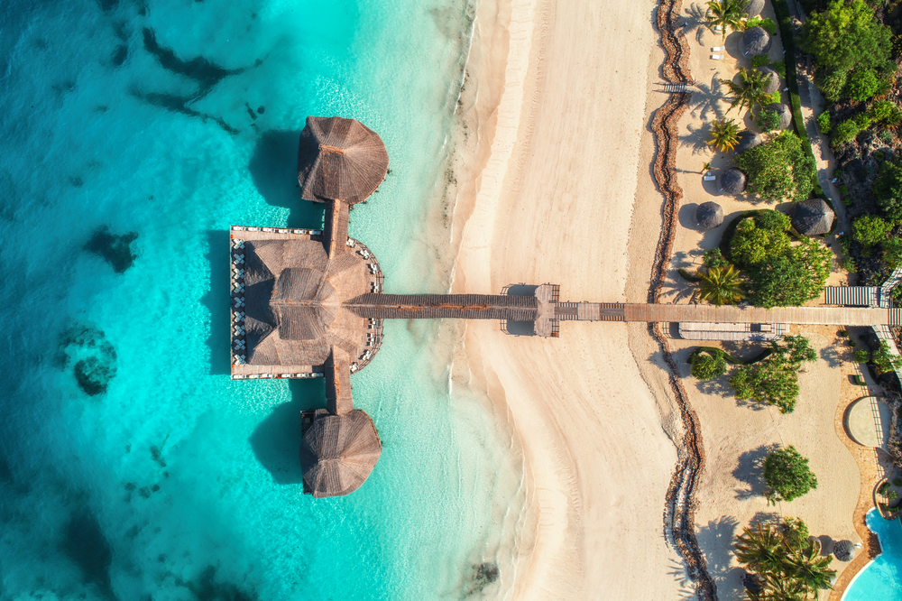 Aerial view of beautiful hotel in Indian ocean at sunrise in summer. Zanzibar, Africa. Top view.  Building on the sea. Aerial landscape with wooden hotel, clear azure water, sandy beach. Luxury resort
