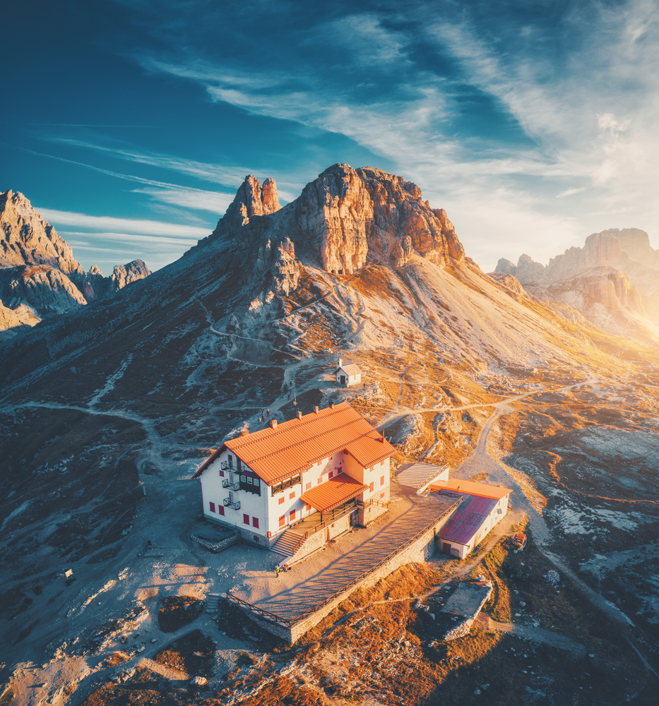 Mountain valley with beautiful house and church at sunset in autumn. Landscape with buildings, high rocks, trail, blue sky and sunlight. Mountains in Tre Cime park in Dolomites, Italy. Italian alps