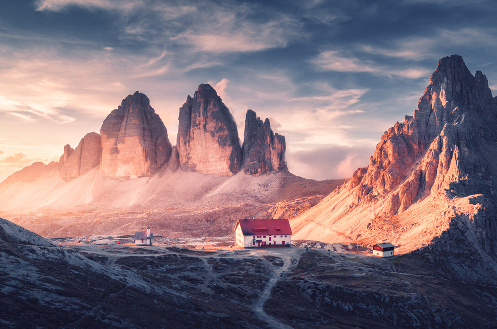 Beautiful house and church in mountain valley at sunset in autumn. Landscape with buildings, high rocks, trail, blue sky and sunlight. Mountains in Tre Cime park in Dolomites, Italy. Italian alps