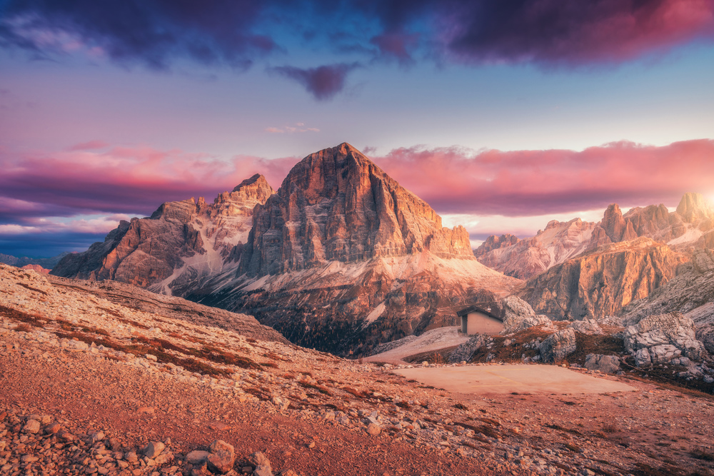 Mountains at sunset in Dolomites, Italy. Landscape with high rocks, stony trail, small house, blue sky with pink clouds in the evening. Autumn scenery with mountain valley. Italian alps at dusk