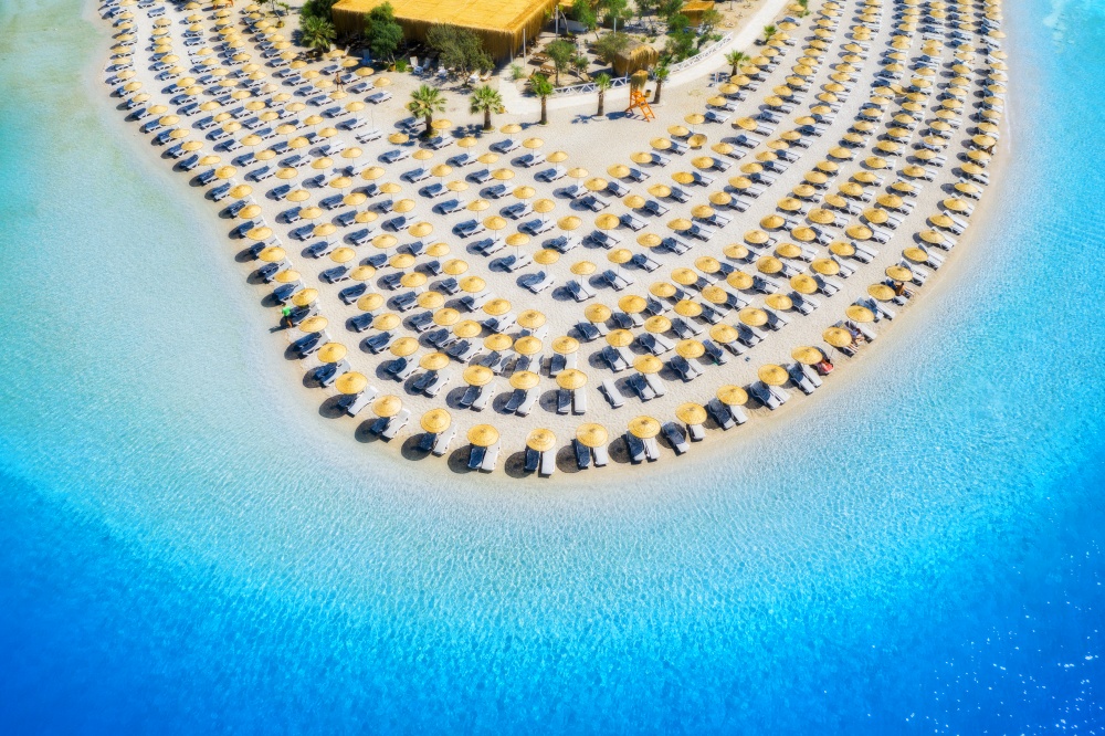 Aerial view of sea, empty sandy beach with sunbeds and umbrellas at sunny day in summer. Blue lagoon in Oludeniz, Turkey. Tropical landscape with clear turquoise water, deck chairs. Travel and leisure