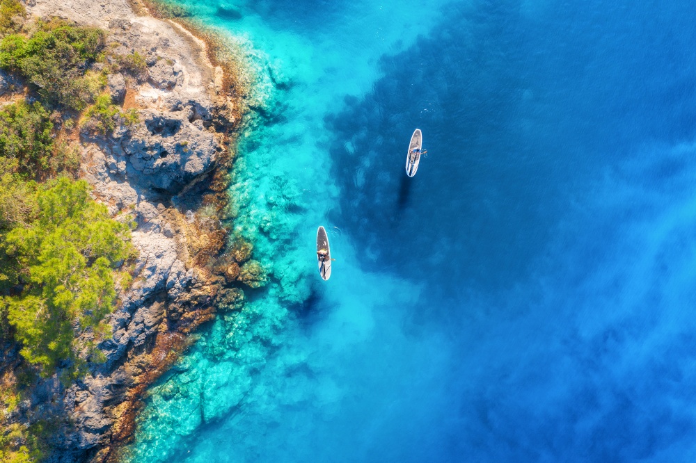 Aerial view of people on floating sup boards on blue sea, rocks, trees at sunset in summer. Blue lagoon, Oludeniz, Turkey. Tropical landscape. Kayaks on clear water. Active travel. Top view of canoe
