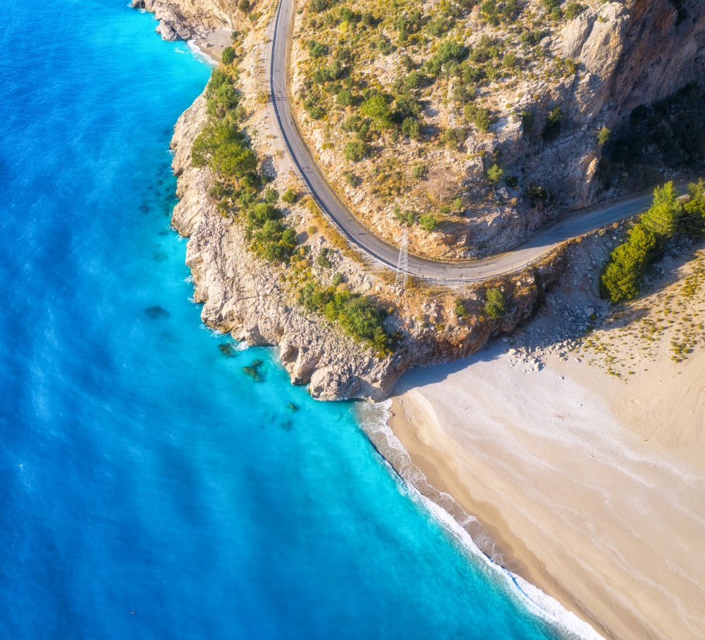 Aerial view of mountain road near blue sea with sandy beach at sunset in summer. Oludeniz, Turkey. Top view of road, trees, blue water, mountain. Beautiful landscape with highway, rocks and sea coast