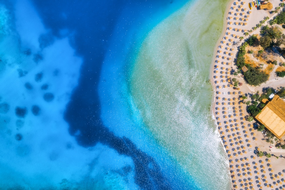 Aerial view of sandy beach with umbrellas, green forest at sunset in summer. Blue lagoon in Oludeniz, Turkey. Tropical landscape with sea bay, island, white sandy bank, blue water. Top view. Nature