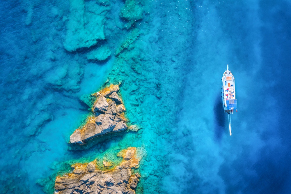 Aerial view of beautiful yacht on the sea and rocks at sunny day in summer in Turkey. Top view of boat, stones, clear blue water. Tropical landscape. Travel. Nature background. View from above. Cruise