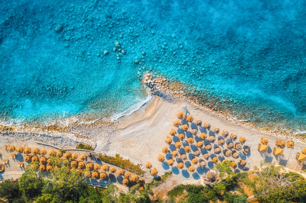 Aerial view of sandy beach with umbrellas, green forest at sunset in summer. Blue lagoon in Oludeniz, Turkey. Tropical landscape with sea bay, island, white sandy bank, blue water. Top view. Nature