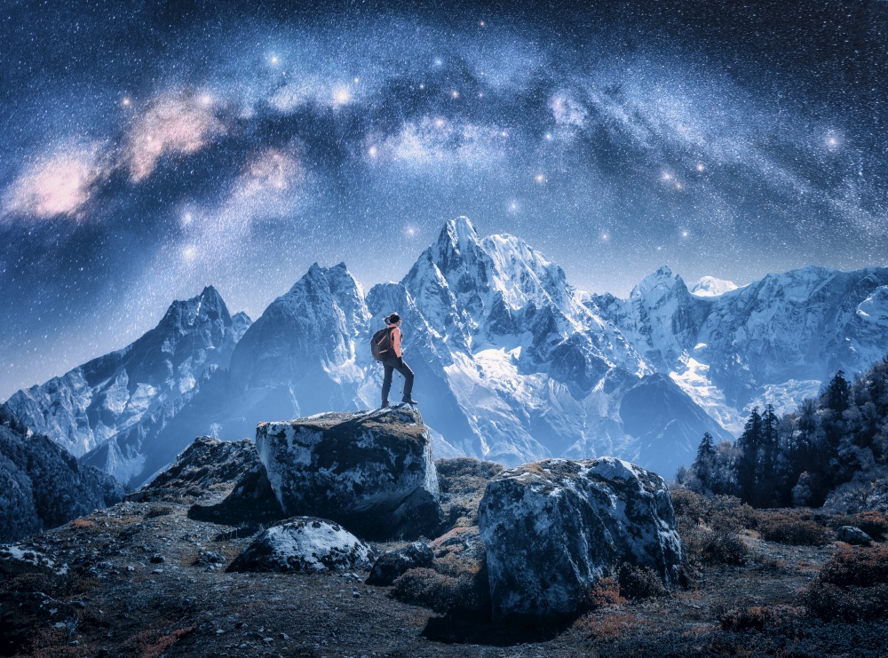 Arched Milky Way and sporty woman on the stone and mountains in snow at night. Girl with backpack, sky with bright stars, snowy rocks in Nepal. Space. Landscape with milky way arch. Travel and hiking