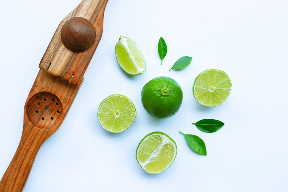 Limes with wooden lime squeezer on white background.