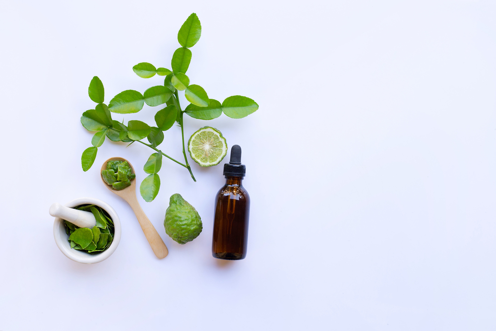 Bottle of essential oil and  fresh kaffir lime or bergamot fruit with leaves isolated on white background.