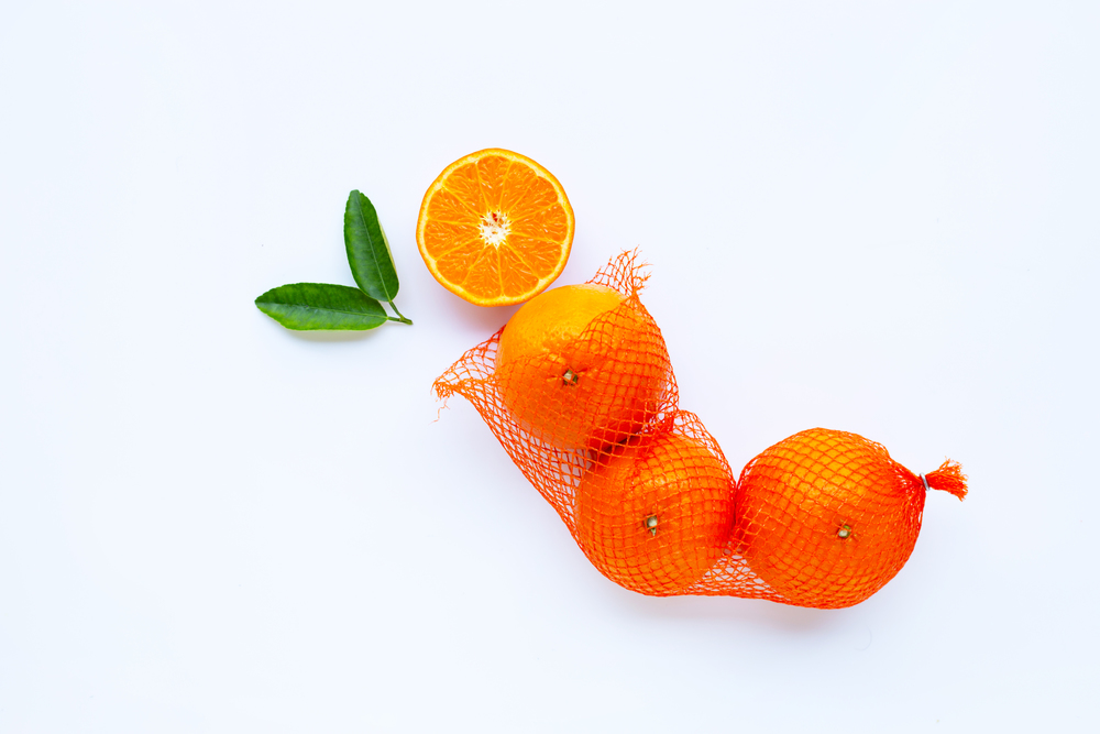 High vitamin C. Orange in net bag with ripe half of orange on white background. Copy space